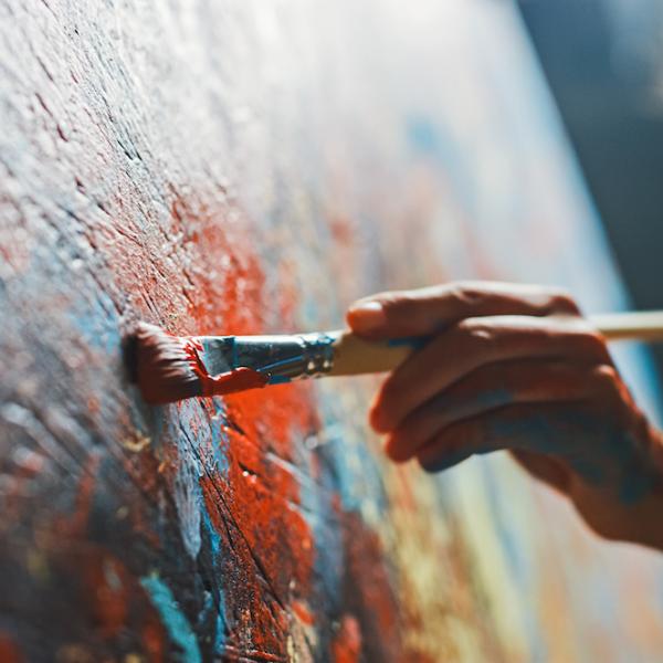 Hand holds a paintbrush to a large red and blue canvas