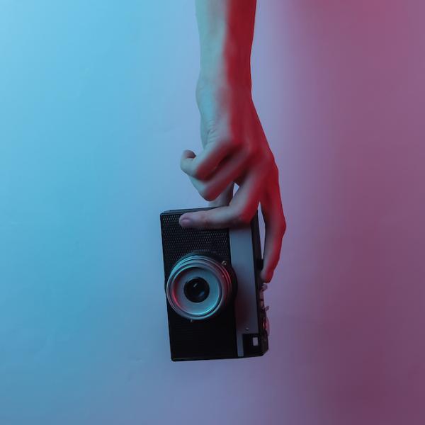 Hand holds a camera against a gradient of blue to magenta